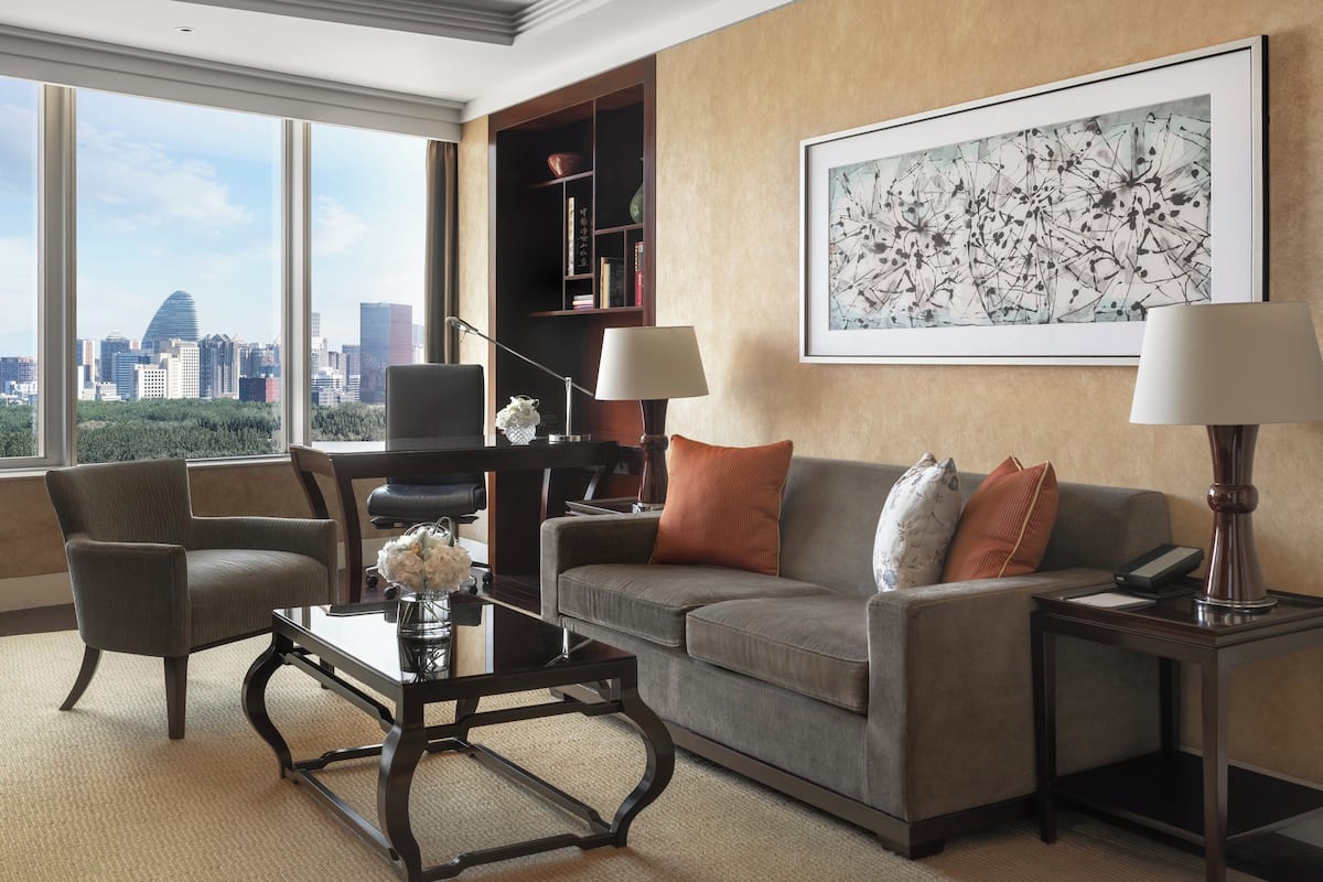 A modern living room with a large window, a sofa, a coffee table, and a bookshelf.