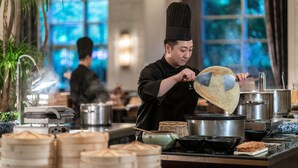 A chef in a black uniform cooking in a professional kitchen with stainless steel appliances and bamboo steamers. - Four Seasons Hotel Beijing (Beijing)