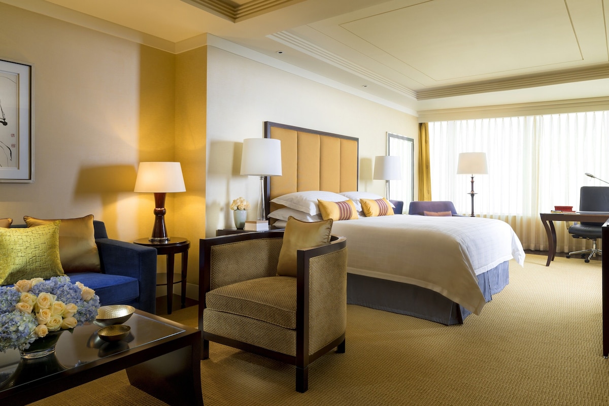 A hotel room with a bed, a desk, a chair, a sofa, and a coffee table.