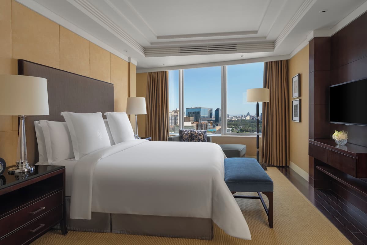 A hotel room with a large bed, bedside tables, a TV, and a view of the city.