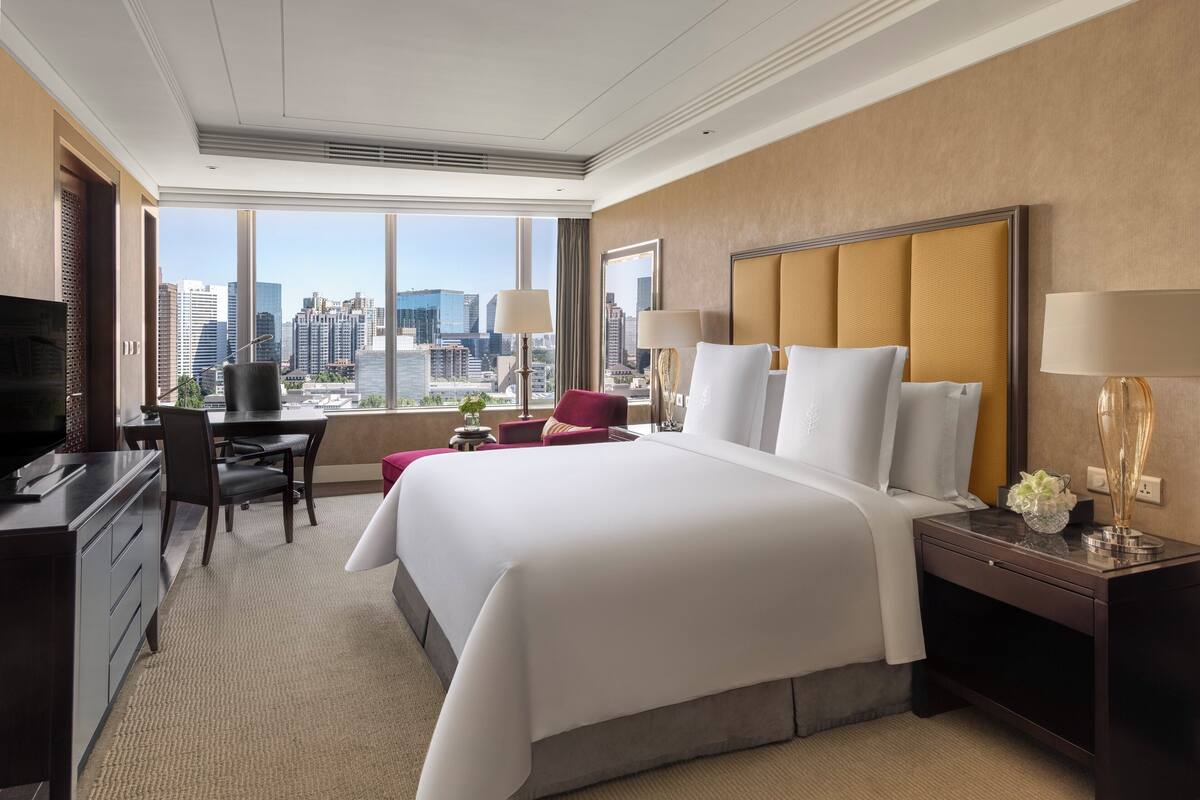 A hotel room with a large bed, a desk, a chair, and a TV.