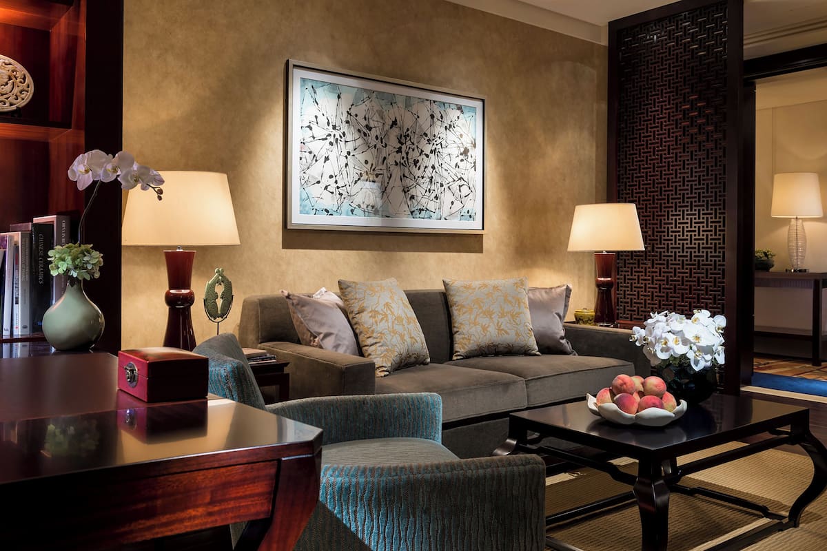 A modern living room with a sofa, armchairs, a coffee table with fruit, and two lamps.