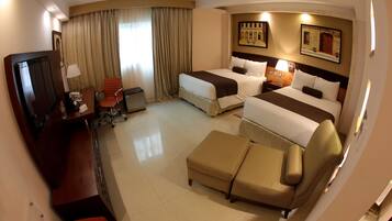A hotel room with two beds, a desk, a TV, a chair, and a sofa.