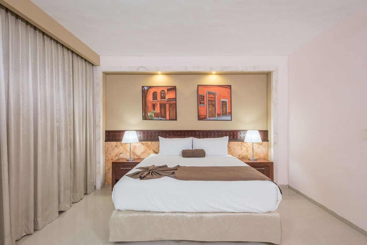A hotel room with a large bed, two bedside lamps, a headboard with a marble-like texture, and two framed pictures on the wall.