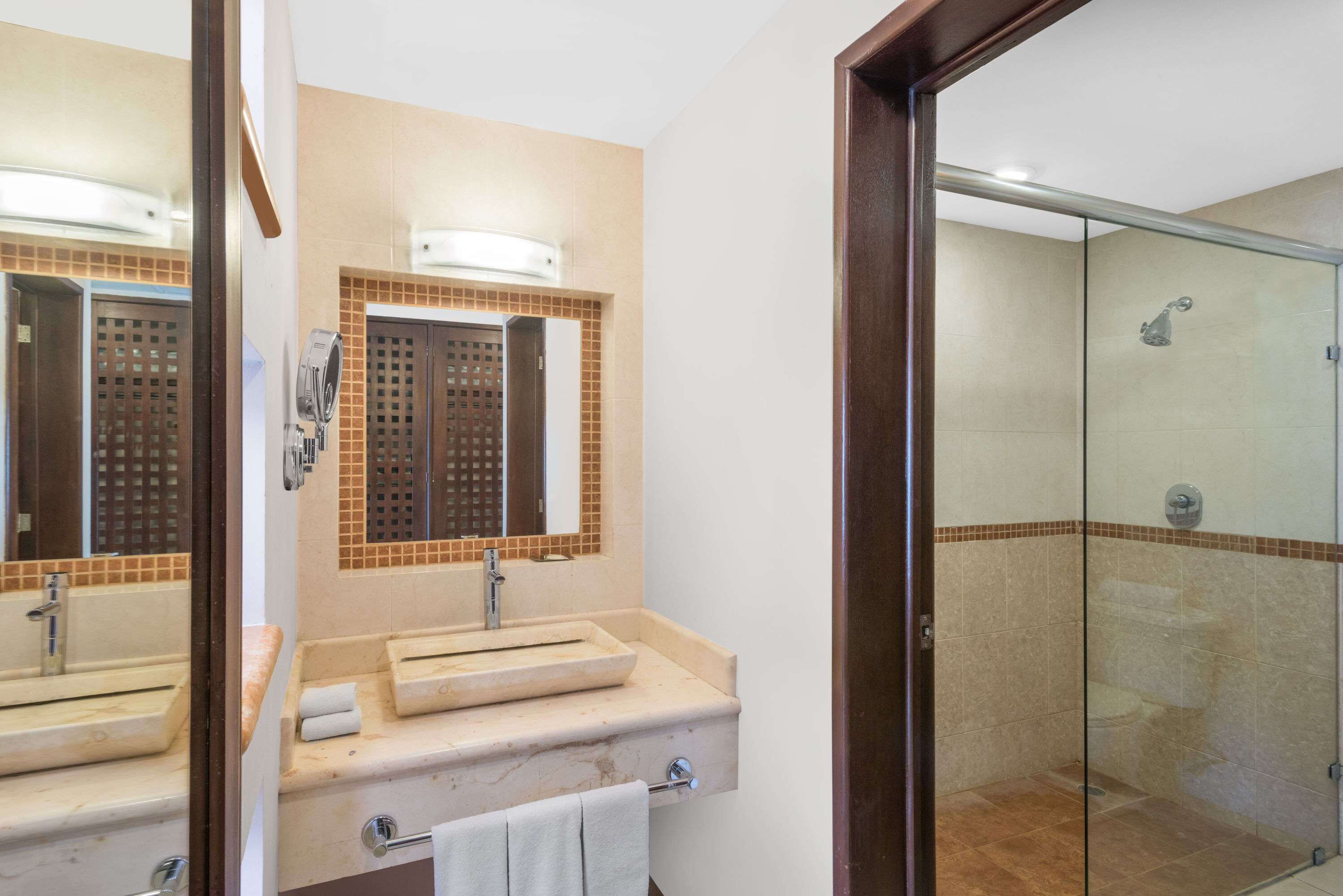 Un baño con un espejo grande, dos lavamanos, una ducha y una puerta de cristal.