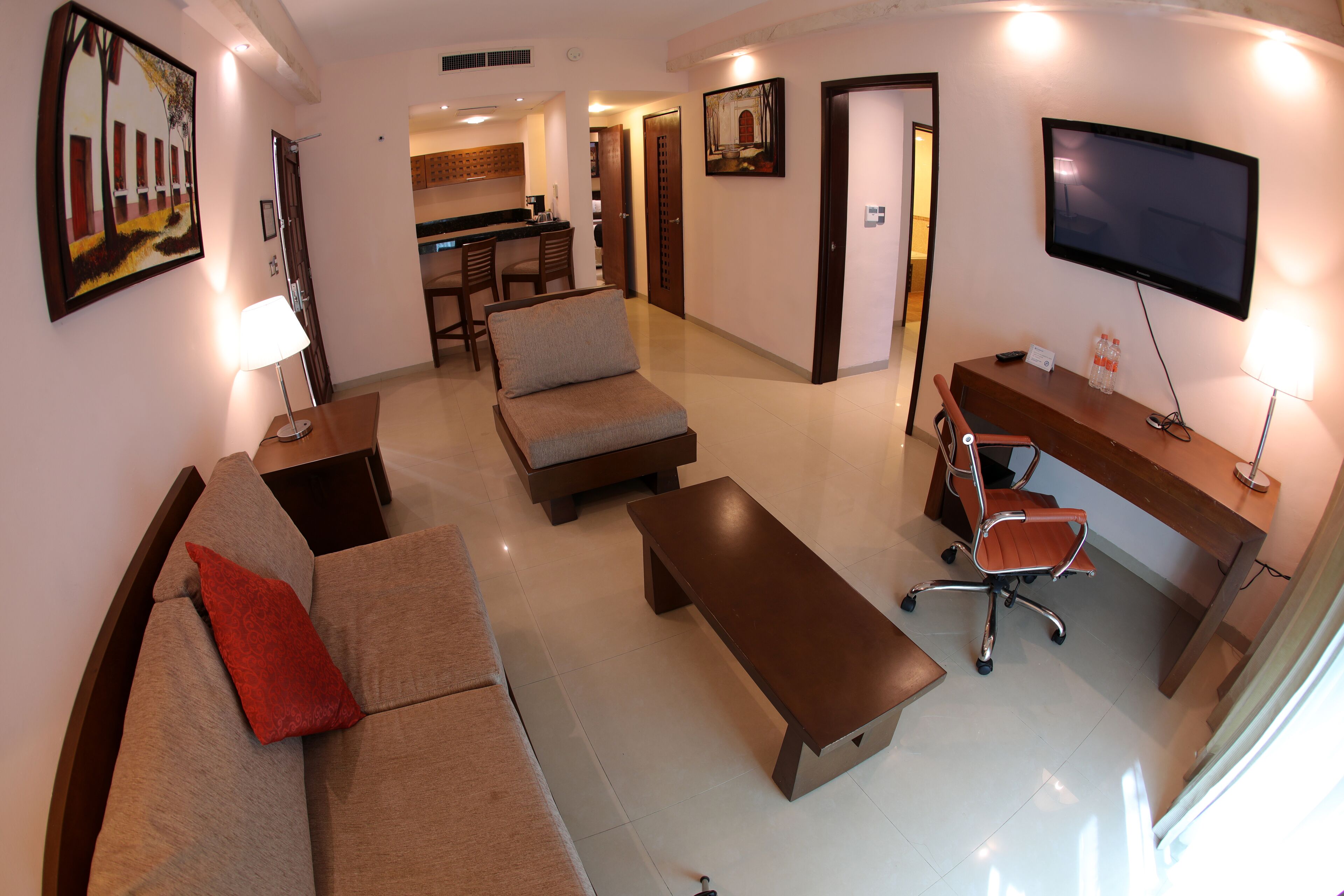 A living room with a sofa, a coffee table, a desk with a chair, and a TV mounted on the wall.