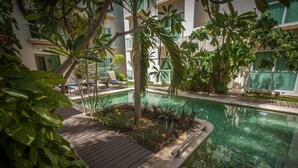 A pool area with a wooden deck, surrounded by lush greenery and a clear pool. - Wyndham Merida (Mérida)