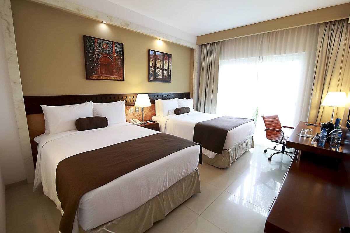 A hotel room with two beds, a desk, and a chair.