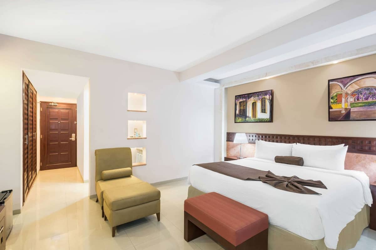 A hotel room with a bed, a chair, a bench, a door, and wall-mounted mirrors.