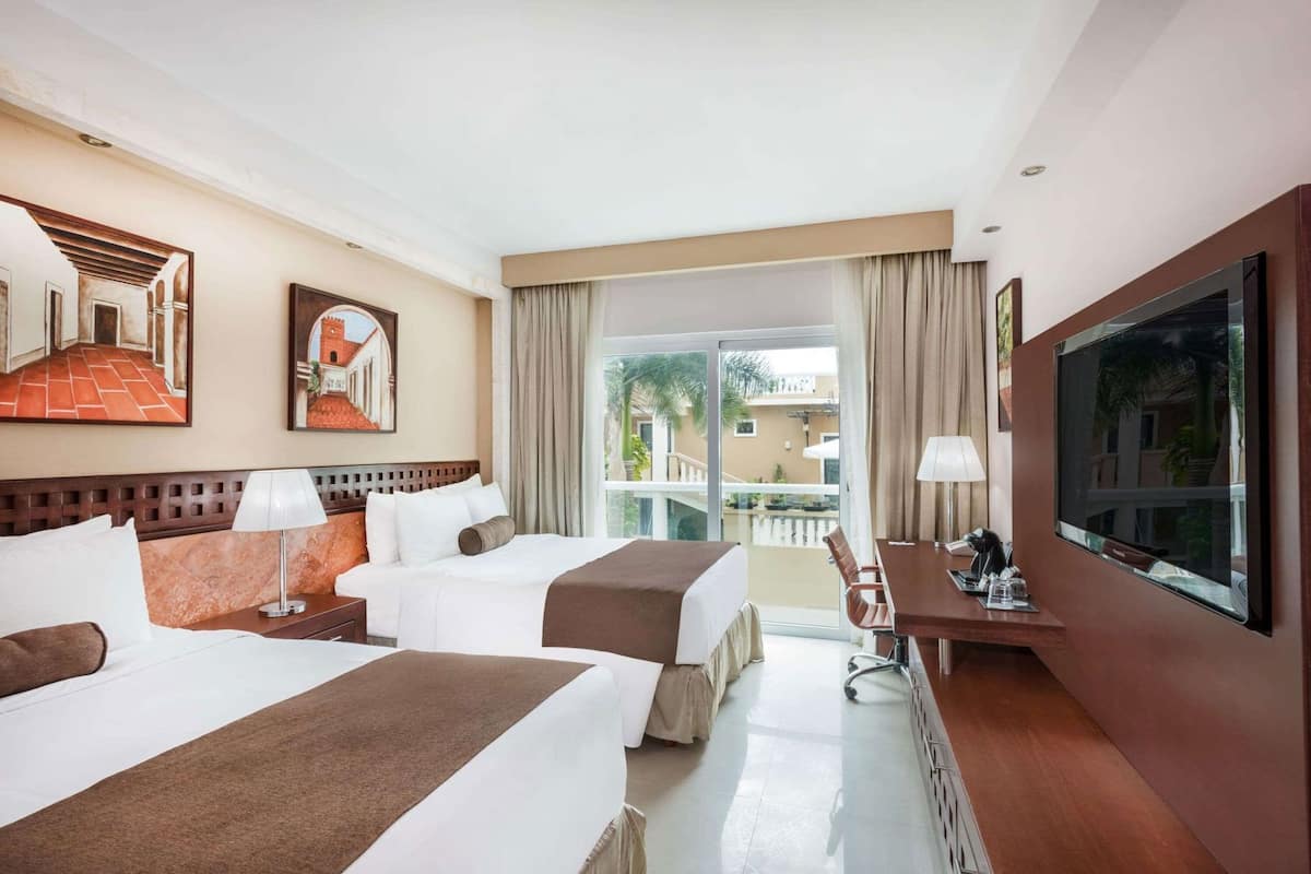 A hotel room with two beds, a desk, a TV, and a balcony with a view.