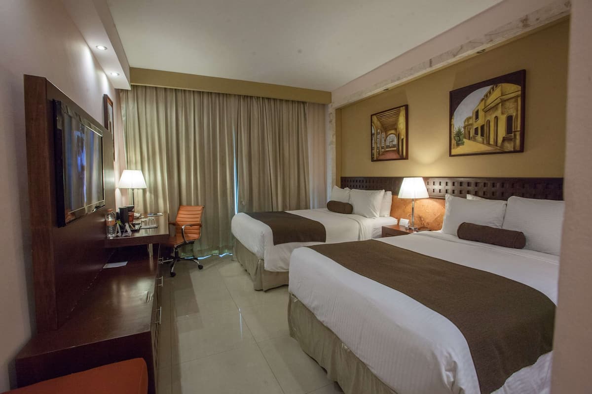 A hotel room with two beds, a desk, a chair, a TV, and a window with curtains.