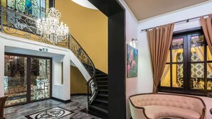 A grand staircase with a chandelier, a plush armchair, and a painting on the wall. - Wyndham Merida (Mérida)