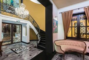 A grand staircase with a chandelier, a plush armchair, and a painting on the wall.