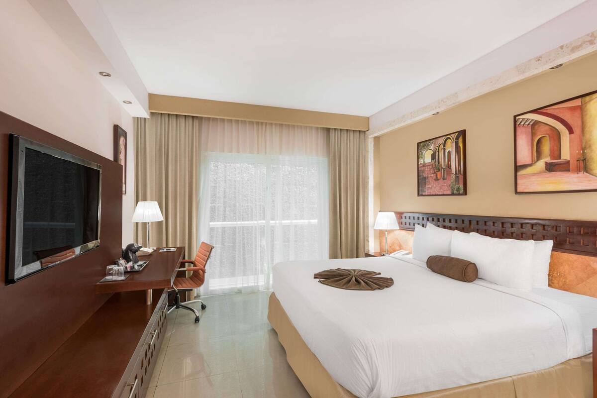A hotel room with a large bed, a desk, a television, and a window with curtains.