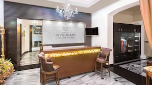 A reception area with a chandelier, a reception desk, and a TV screen. - Wyndham Merida (Mérida)