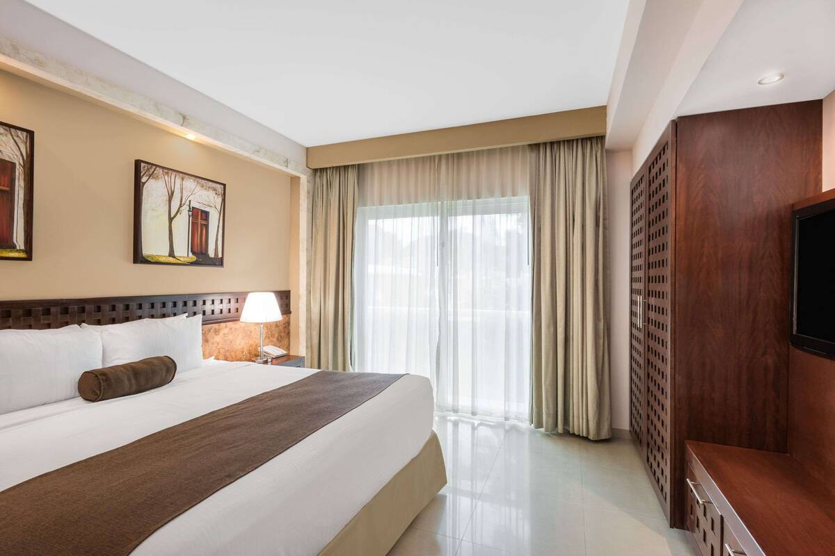 A hotel room with a large bed, a TV, a desk, and a window with curtains.