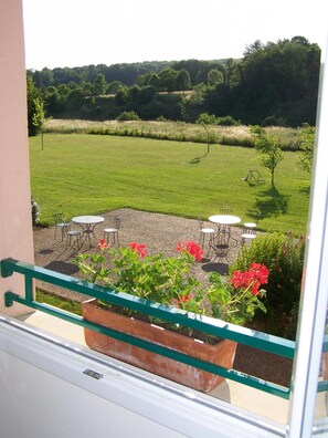 A balcony with a view of a grassy field, outdoor seating, and a planter with flowers. - Brit Hotel Du Perche (Nogent-le-Rotrou)