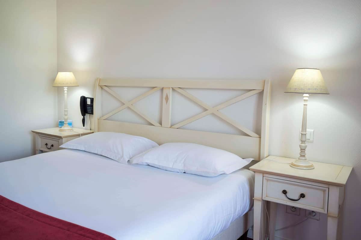 A neatly made bed with white linens and a red blanket, two bedside tables with lamps, and a wall-mounted telephone.