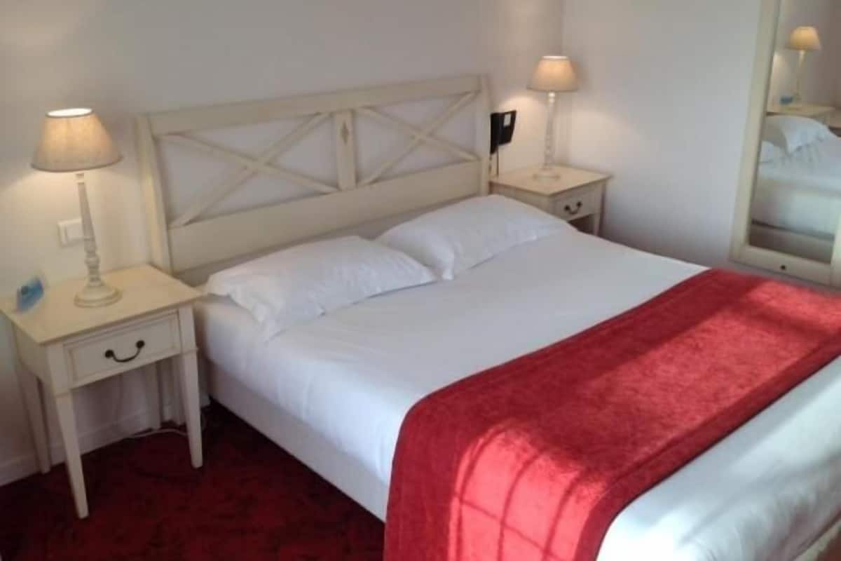 A neatly made bed with white linens and a red blanket, flanked by two bedside tables with lamps, in a room with a simple, clean design.