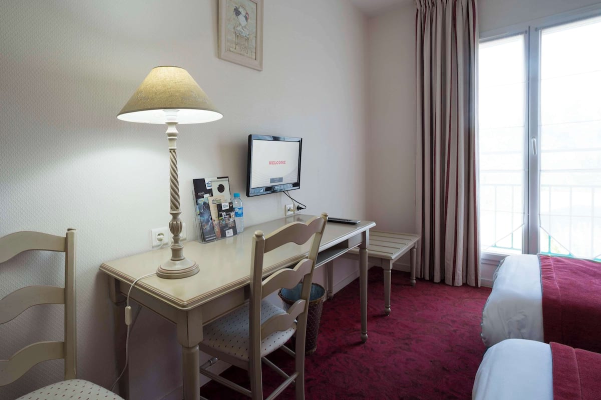 A hotel room with a desk, a chair, a bed, a TV, and a window with curtains.