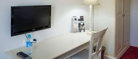 Habitación de hotel con escritorio, silla, televisor, lámpara y armario.