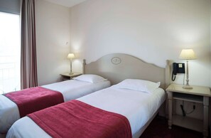 A hotel room with two beds, each with a red blanket, bedside tables with lamps, and a wall clock. - Brit Hotel Du Perche (Nogent-le-Rotrou)