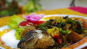 A plate of food with a fish and vegetables on a table with a yellow tablecloth.