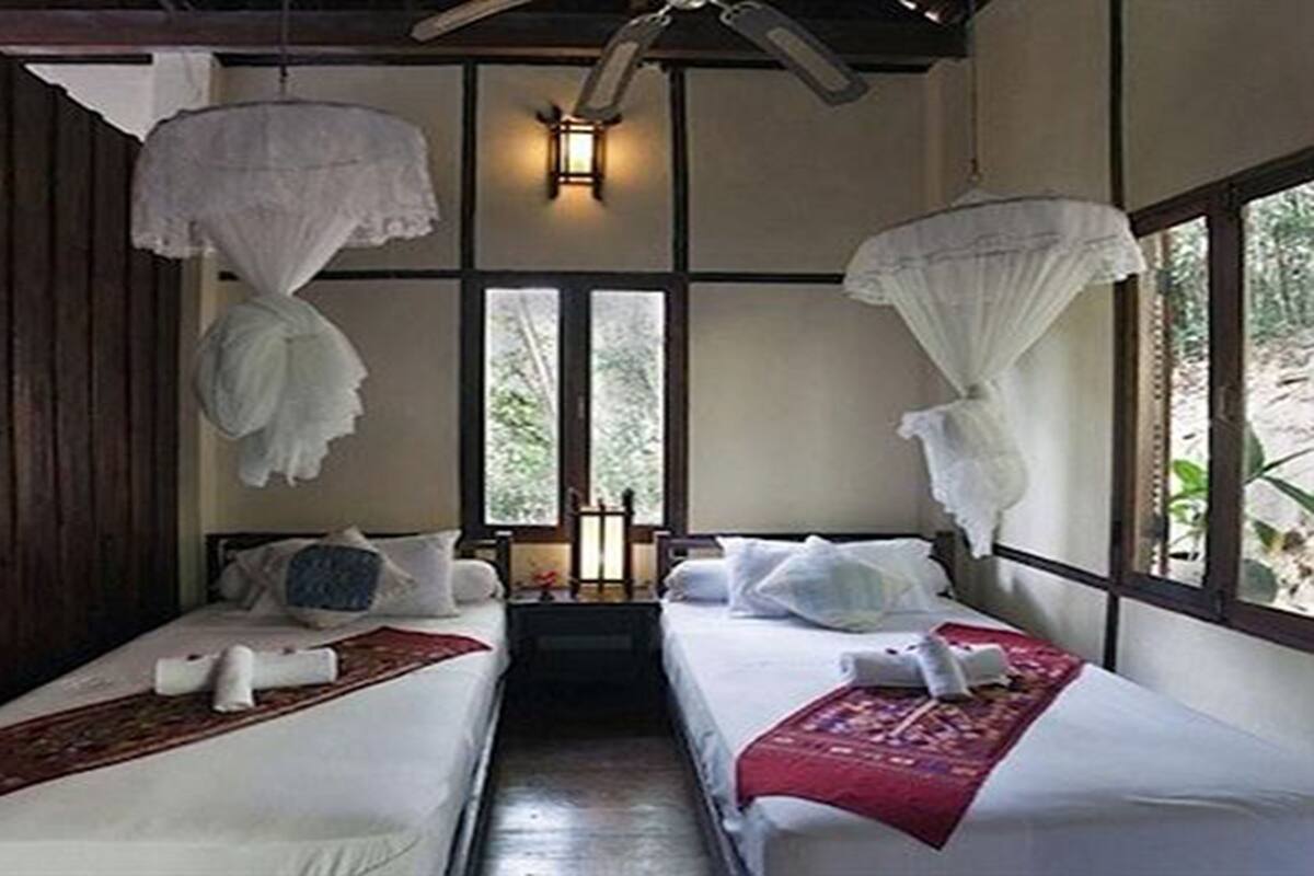 Une chambre avec deux lits, un plafond en bois, une lanterne et une vue sur la verdure environnante.