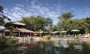 Un cadre paisible au bord du lac, avec des constructions aux toits de chaume et des parasols, le tout entouré d’une végétation luxuriante.