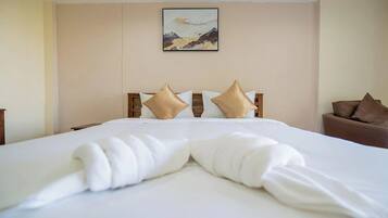 A hotel room with a neatly made bed, a painting on the wall, and a brown armchair.