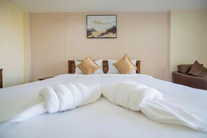 A hotel room with a neatly made bed, a painting on the wall, and a brown armchair. - Hillside Resort (Pattaya)