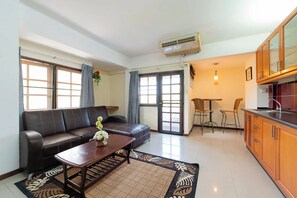 A living room with a sofa, coffee table, and a rug. There is a kitchen area with wooden cabinets and a dining table with chairs. - Hillside Resort (Pattaya)