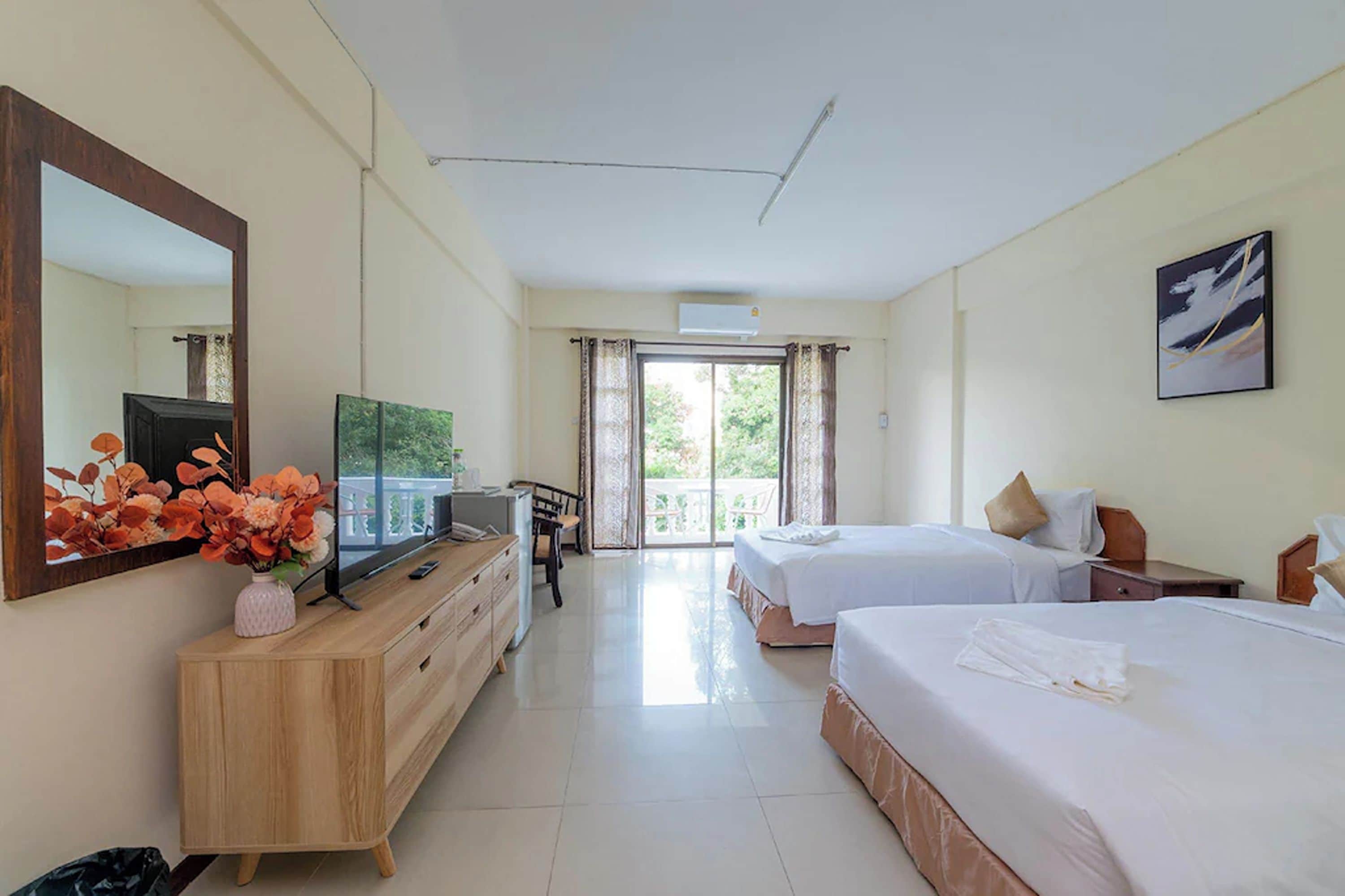 A hotel room with a large bed, a smaller bed, a desk with a TV, a dresser, and a large window with curtains.