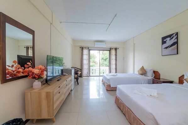A hotel room with a large bed, a smaller bed, a desk with a TV, a dresser, and a large window with curtains.