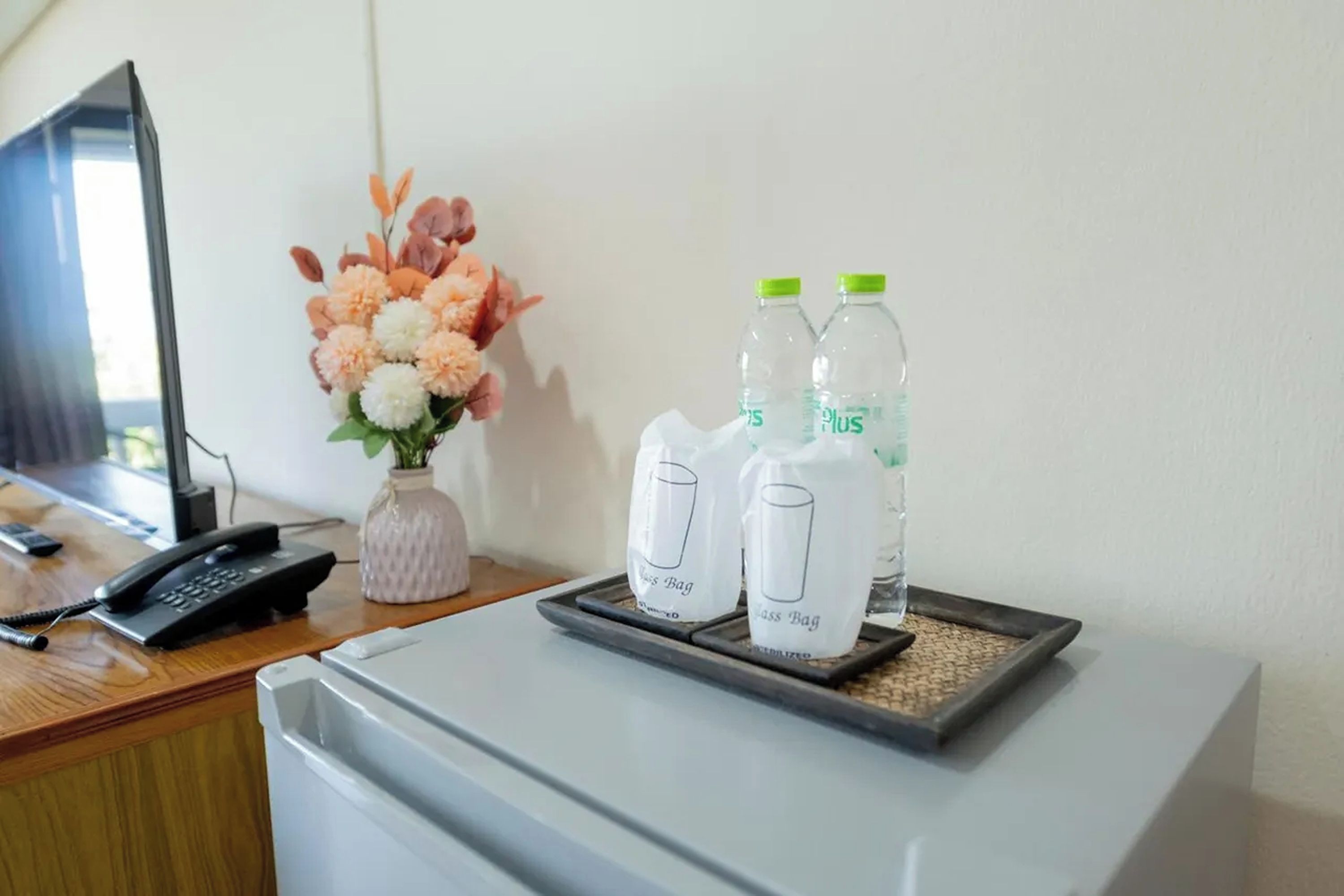 A hotel room with a desk, a vase of flowers, and two bottles of water on a tray.