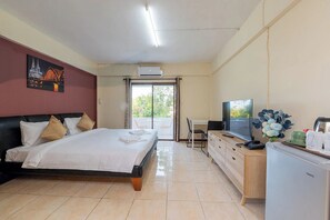 A hotel room with a bed, a desk, a television, and a view of the outdoors. - Hillside Resort (Pattaya)