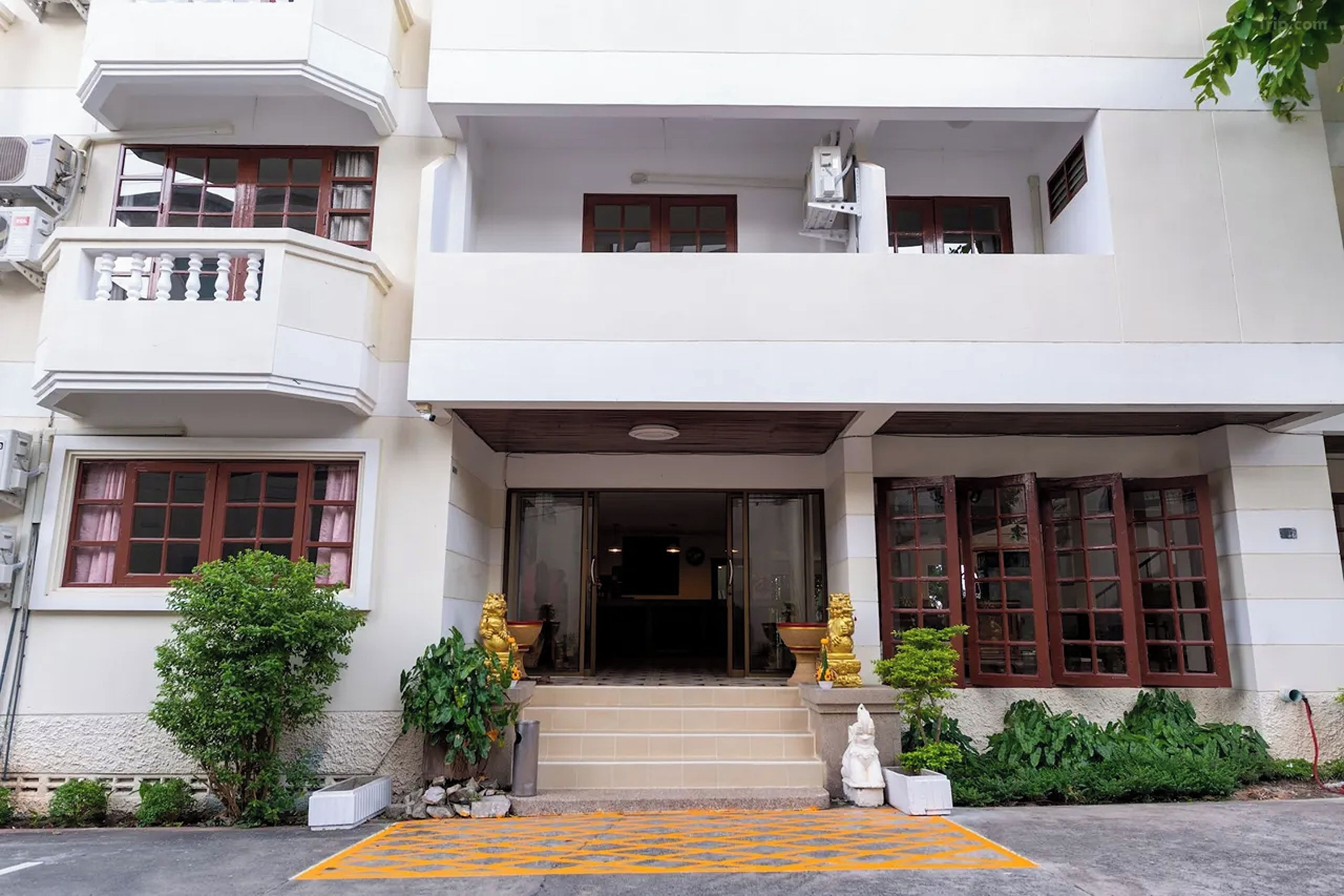 A two-story building with a balcony, a set of stairs leading to the entrance, and a small garden area with statues.
