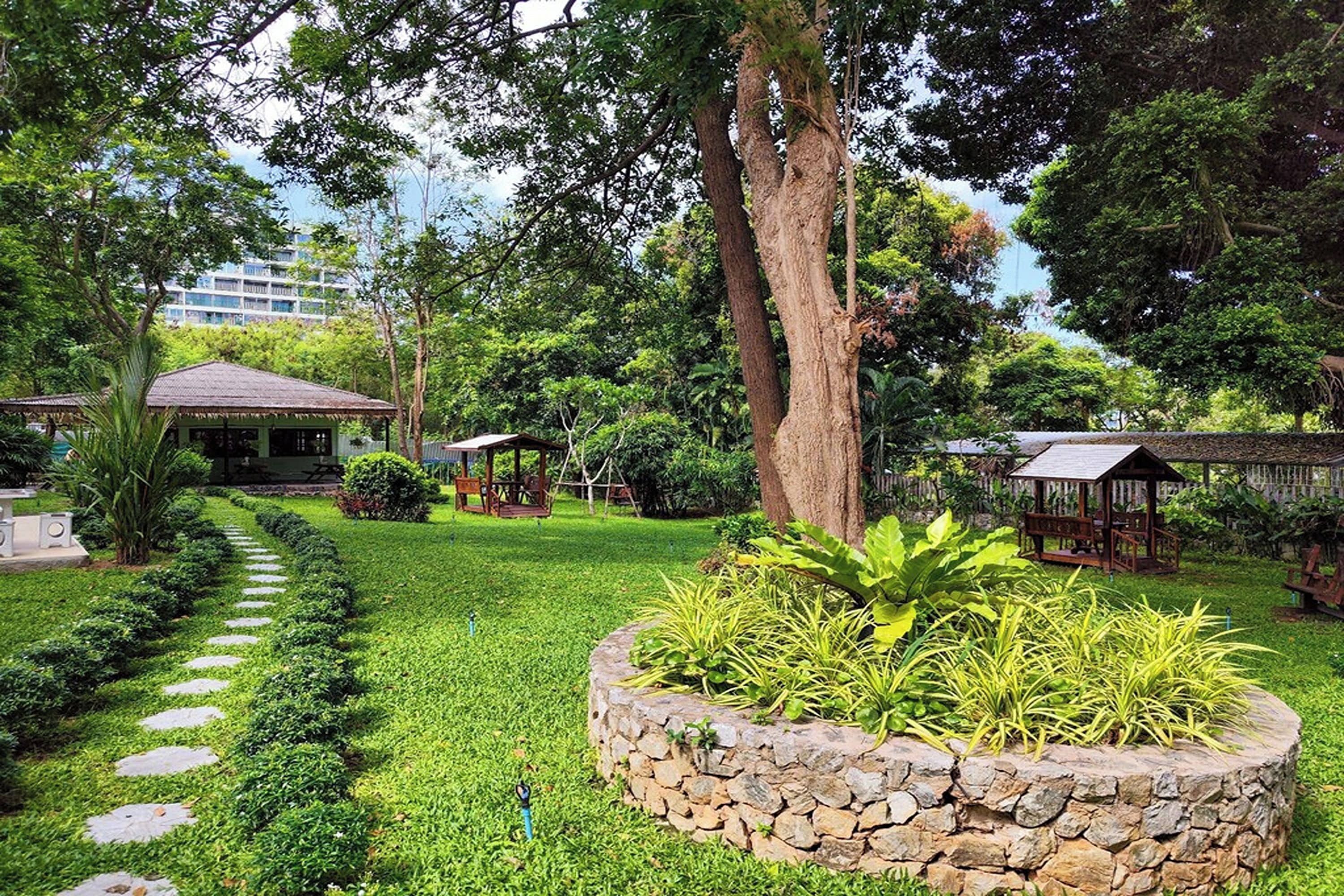 A well-maintained garden with a stone pathway, lush greenery, and wooden structures.