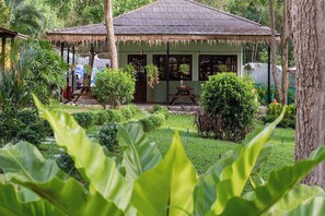Une hutte traditionnelle avec un toit de chaume, entourée d’une végétation luxuriante et d’un jardin bien entretenu.