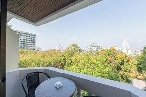 A balcony with a round table and two chairs, overlooking a cityscape with buildings and trees. - Hillside Resort Pattaya (Pattaya)