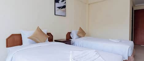 Quarto de hotel com duas camas, cada uma com cabeceira de madeira, roupa de cama branca e travesseiro marrom. Um quadro emoldurado está pendurado na parede acima das camas.
