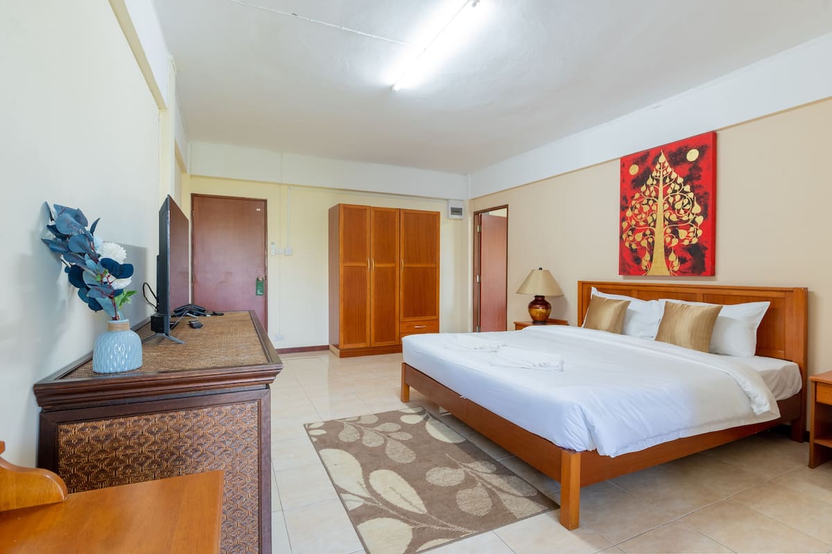 A bedroom with a bed, wardrobe, desk, lamp, and artwork.