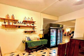 A kitchen with a refrigerator, shelves with bottles, a table with a tablecloth, and a patterned floor. - Hillside Resort Pattaya (Pattaya)