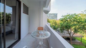 A balcony with a glass door, a small round table with a chair, and a view of a building and trees. - Hillside Resort Pattaya (Pattaya)