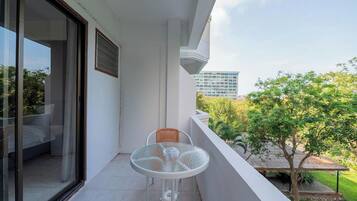 A balcony with a glass door, a small round table with a chair, and a view of a building and trees.