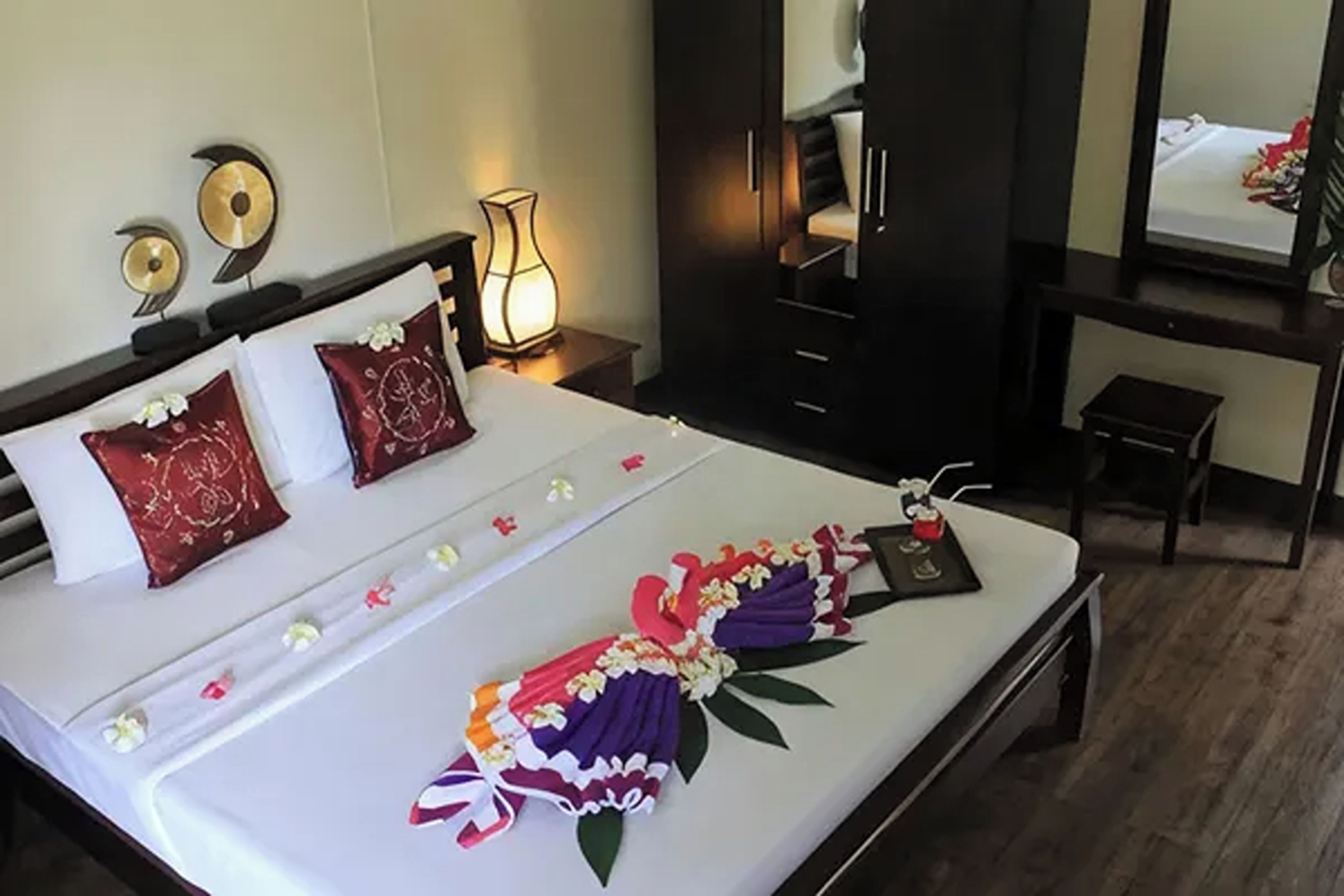 A hotel room with a neatly made bed, a bedside lamp, a mirror, and a small table with a bottle.