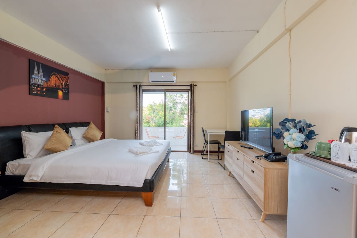 A hotel room with a bed, a desk with a computer, a TV, and a refrigerator.