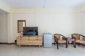 A hotel room with a wooden cabinet, a flat-screen TV, a small refrigerator, two wicker chairs, and a mirror on the wall. - Hillside Resort (Pattaya)