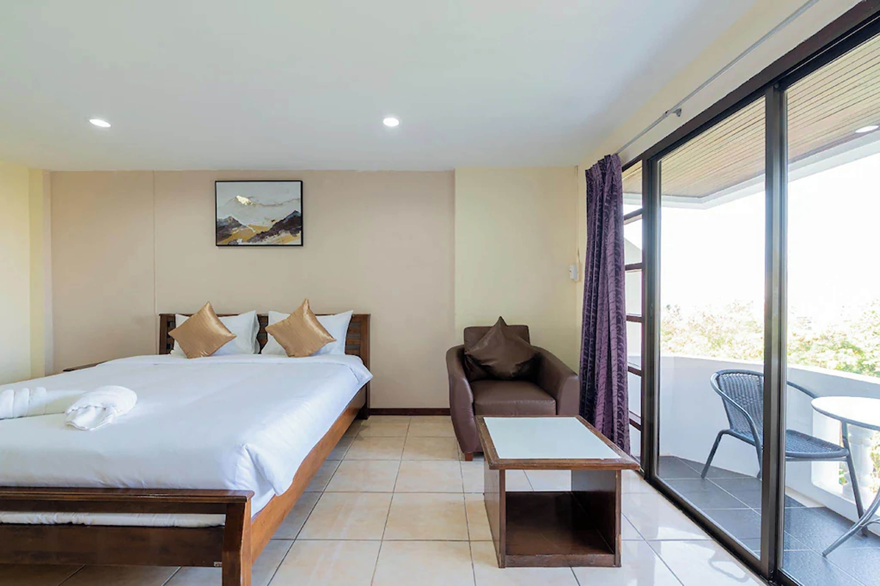 A hotel room with a bed, a sofa, a small table, and a balcony with a chair.