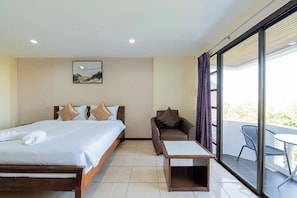 A hotel room with a bed, a sofa, a small table, and a balcony with a chair.